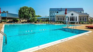 En swimmingpool med kristallklart blått vatten, omgiven av en terrass av tegel och solstolar.