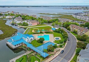 A large house with a blue roof, a swimming pool, and a dock extending into a lake. - North OC 2 Bedroom Condo with Pool! Harbour Club #12G (Ocean City)