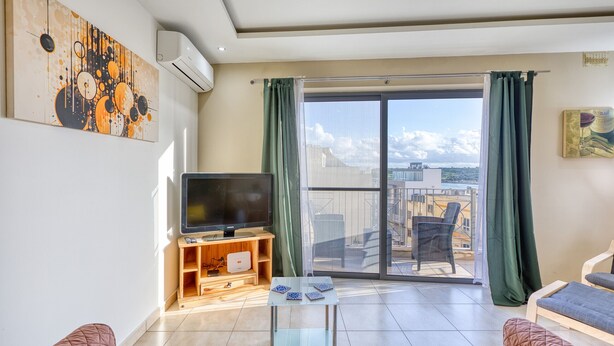 Un salon moderne doté d’un téléviseur à écran plat, d’une petite table agrémentée d’objets décoratifs, d’un canapé et d’un balcon offrant une vue sur la ville.