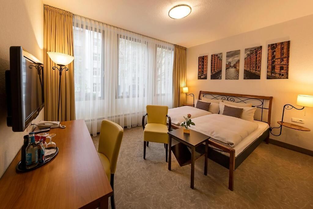 A hotel room with a bed, a desk, a chair, a TV, and a window with curtains.