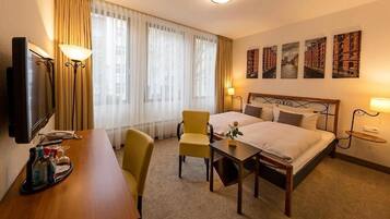 A hotel room with a bed, a desk, a chair, a TV, and a window with curtains.