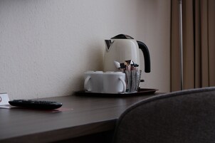 Ein Hotelzimmer mit Kaffeemaschine, Fernbedienung und Tablett mit Tassen und Beilagen auf einem Holztisch.