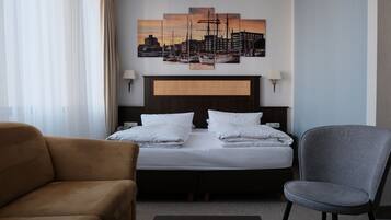 Une chambre d’hôtel avec un lit, un fauteuil marron, un fauteuil gris et un tableau représentant un paysage urbain accroché au mur.