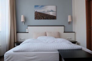 Ein Hotelzimmer mit einem Bett, zwei Nachttischen, einer Wandlampe und einem Bild mit Strandmotiv.