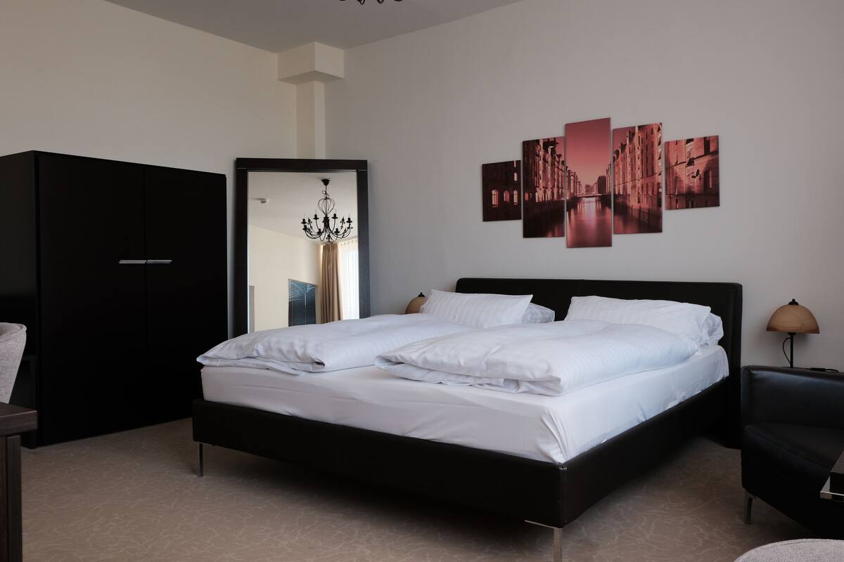 Une chambre moderne avec un grand lit, une armoire, un lustre et un mur orné de trois tableaux encadrés.