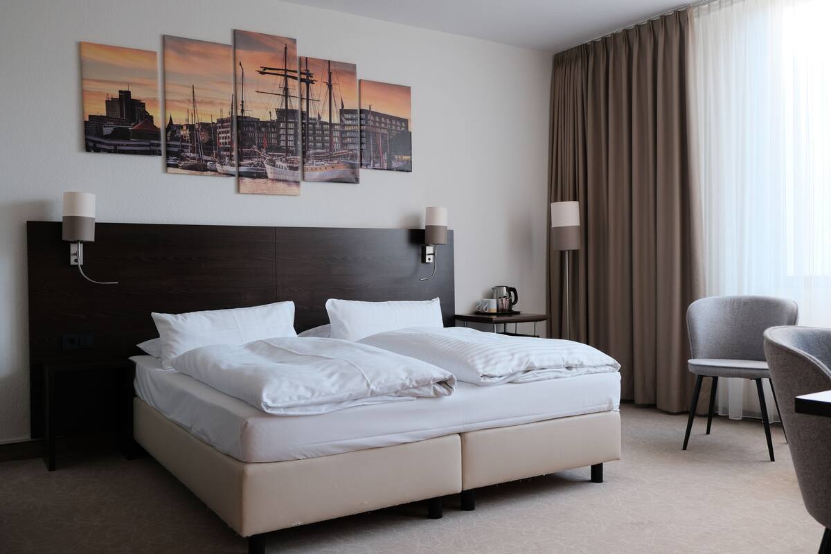 Une chambre d’hôtel avec un lit, deux tables de chevet, une chaise et un mur orné de trois tableaux.