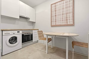 A compact kitchen with a washing machine, oven, and a dining table with chairs. - Cream Lavapiés II (Madrid)