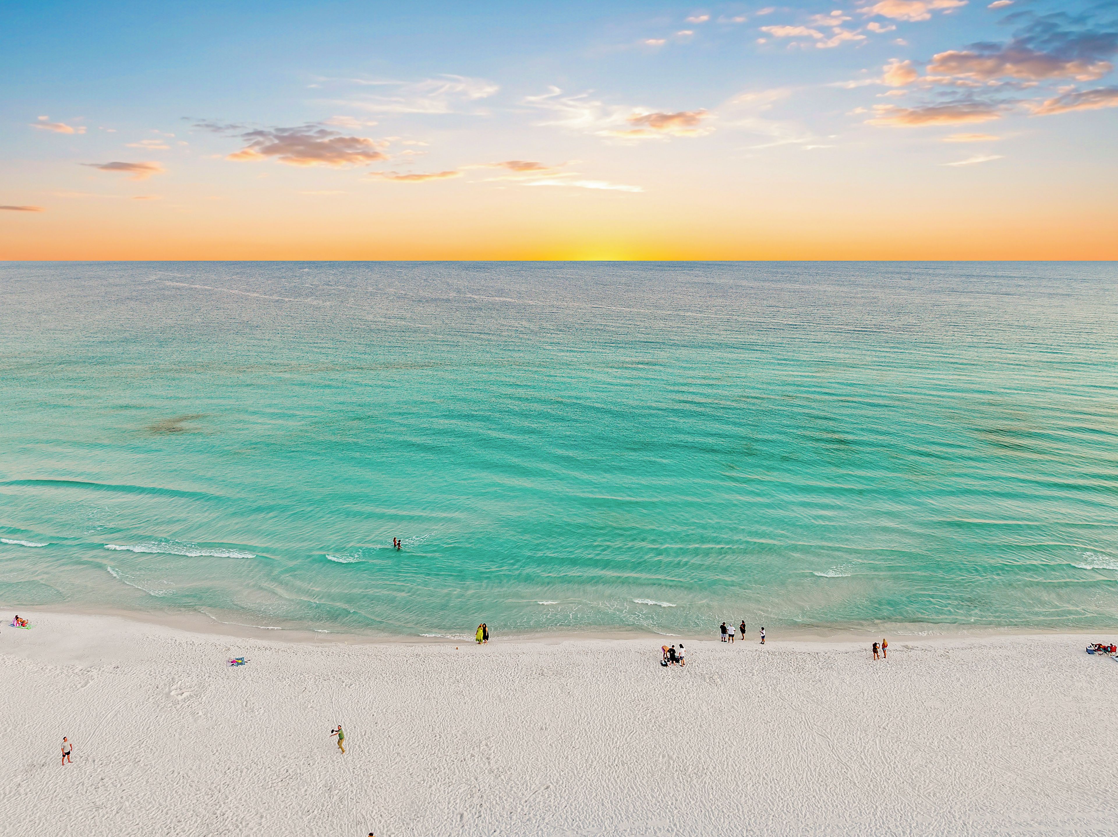 Une plage à l’eau turquoise et limpide, avec un coucher de soleil en toile de fond.