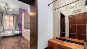 A hotel room with a wooden floor, a bed with a grey headboard, a large mirror, and a wardrobe. - Functional Studio in the Heart of Poznań | 3 min to Market Square (Poznań)