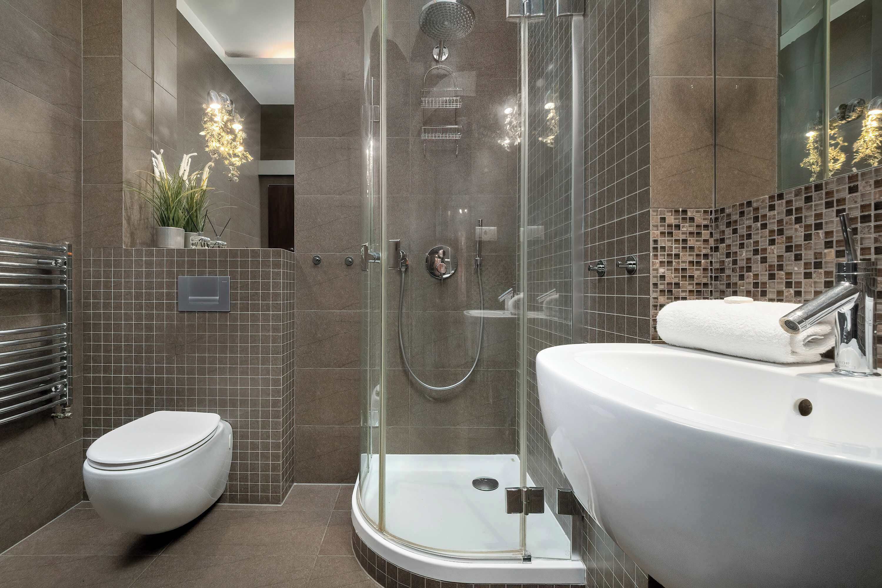 Ein modernes Badezimmer mit einer gläsernen Duschkabine, einer weißen Toilette und einem großen Waschbecken mit Handtuch.