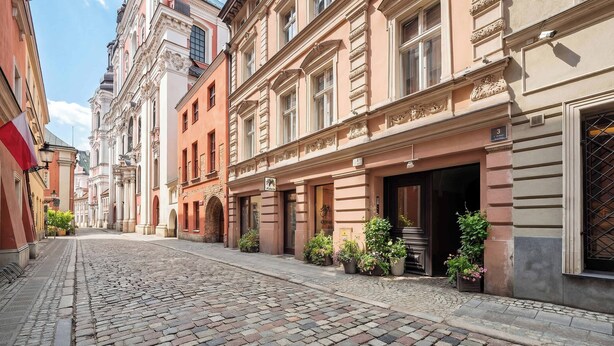 A cobblestone street lined with historic buildings, some with shop fronts and potted plants. - Functional Studio in the Heart of Poznań | 3 min to Market Square (Poznań)