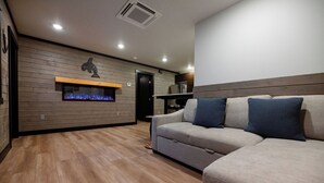 A modern living room with a wooden floor, a sofa with blue cushions, a fireplace, and a kitchen area in the background. - ATI Unit B: 1  BR, 1  BA Duplex in Sitka, Sleeps 3 (Sitka)