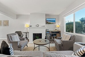 Ein Wohnzimmer mit Kamin, zwei Sesseln, einer Couch, einem Couchtisch und einem Bücherregal.