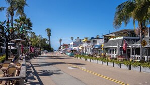 Una strada costiera fiancheggiata da tavoli all'aperto e palme, che conduce a un edificio con il cartello 'Kona Town & Restaurant'.