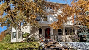 A two-story house with a front porch, a red door, and a staircase leading to the entrance.