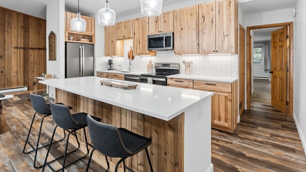 A modern kitchen with wooden cabinets, a large island, bar stools, and pendant lighting. - Buffalo Mtn Views - Spacious Dillon Retreat (Dillon)