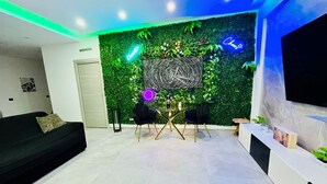 A modern living room with a green wall, a black sofa, a dining table with chairs, and a TV mounted on the wall. - Milano Bicocca Apartment & Rooms (Cinisello Balsamo)