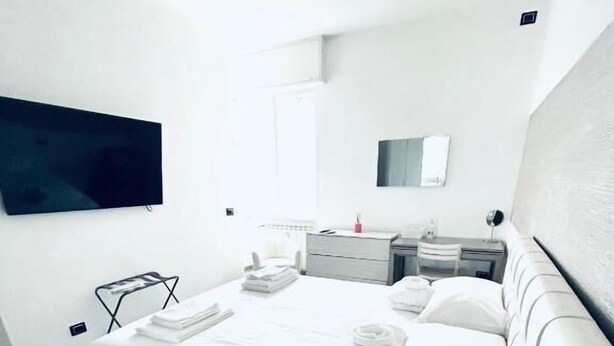 A modern hotel room with a large bed, a flat-screen TV mounted on the wall, a bedside table, and a small seating area. - Milano Bicocca Apartment & Rooms (Cinisello Balsamo)