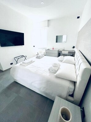 A modern hotel room with a large bed, a flat-screen TV mounted on the wall, a bedside table, and a small seating area. - Milano Bicocca Apartment & Rooms (Cinisello Balsamo)