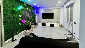A modern living room with a green wall, a flat-screen TV, a white console table, and a black sofa. - Milano Bicocca Apartment & Rooms (Cinisello Balsamo)