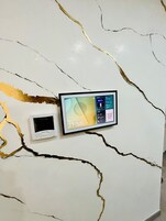 Una pared con diseño de mármol blanco con vetas doradas, un reloj digital enmarcado que muestra la hora, y un dispositivo digital más pequeño debajo.