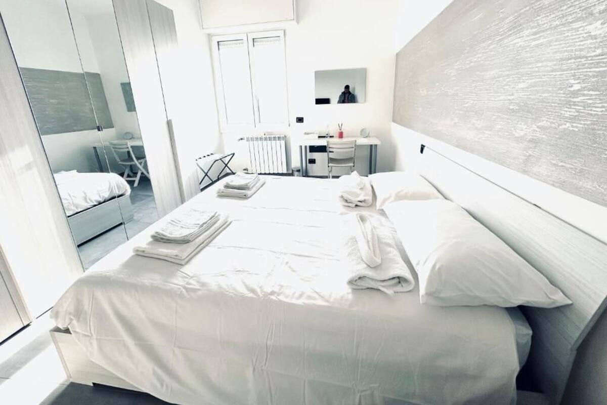 Une chambre d’hôtel moderne avec un grand lit, un bureau et une chaise. On y trouve un miroir, un radiateur et une œuvre d’art accrochée au mur.