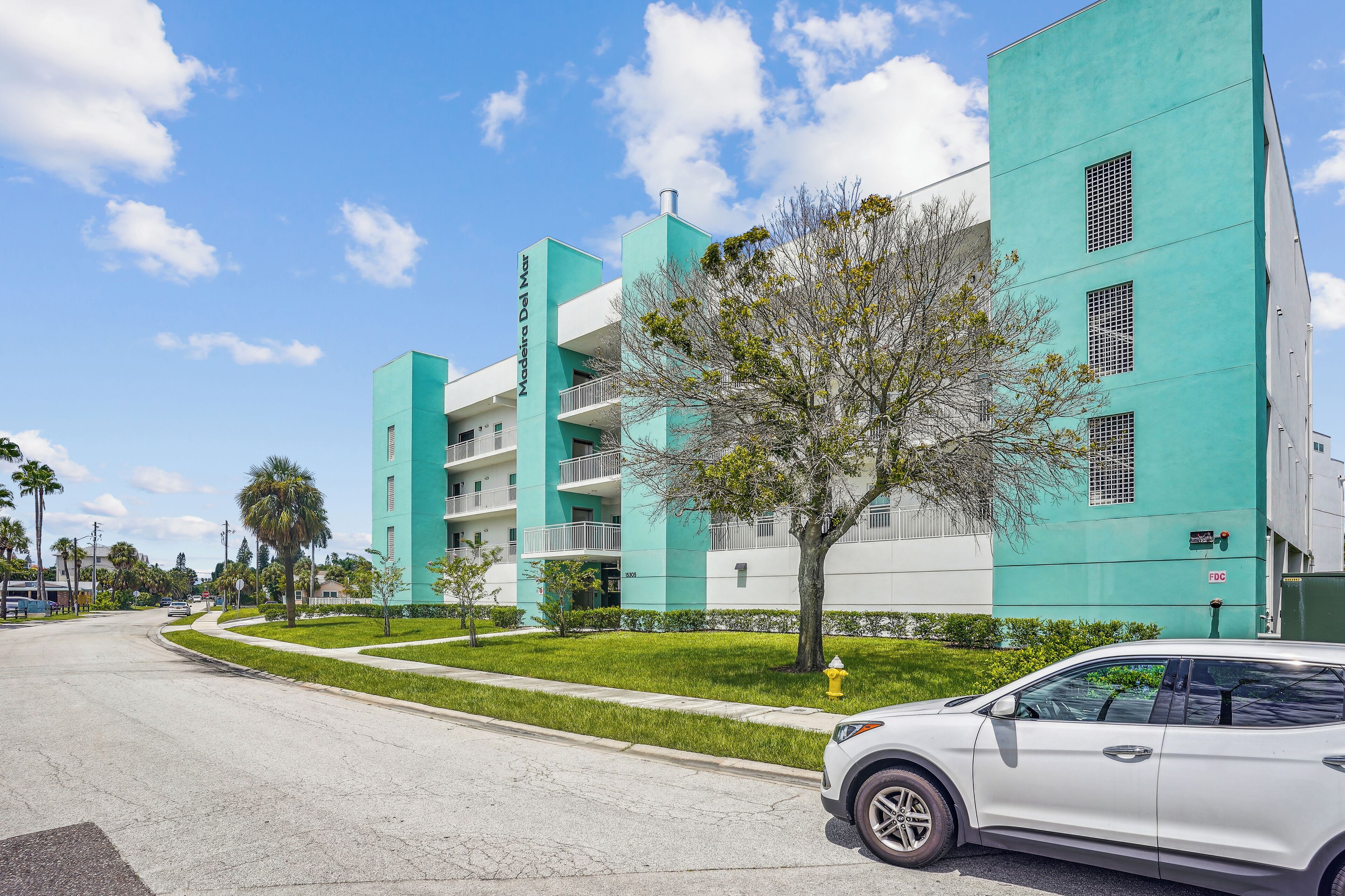 A modern building with a teal facade, multiple balconies, and a well-maintained lawn.