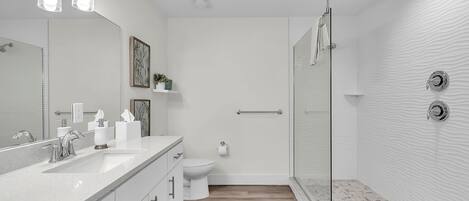 A modern bathroom with a large mirror, a shower, and a toilet.