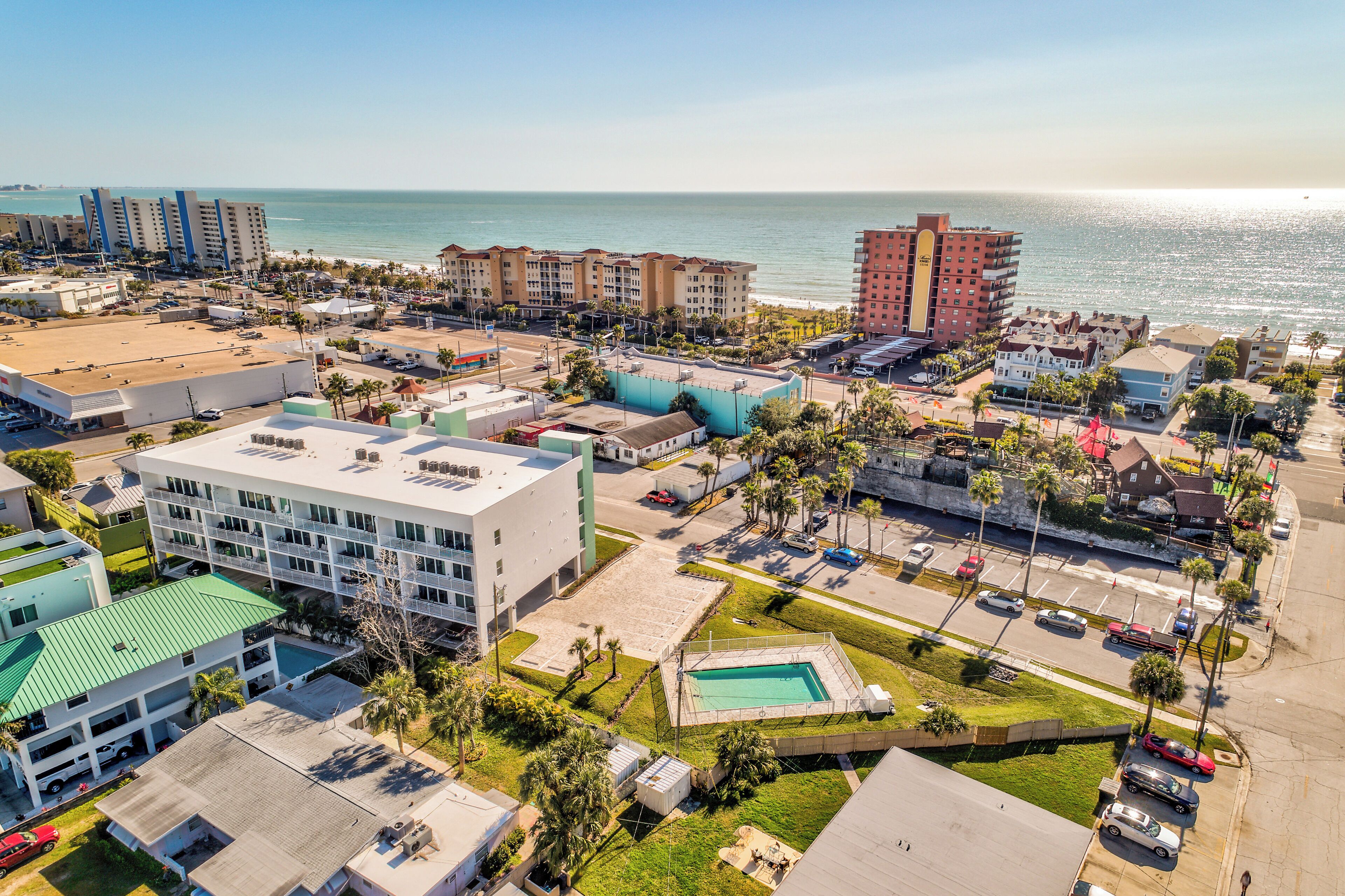 Vue aérienne d’un complexe hôtelier situé sur la côte, avec plusieurs bâtiments, une piscine et une plage en arrière-plan.