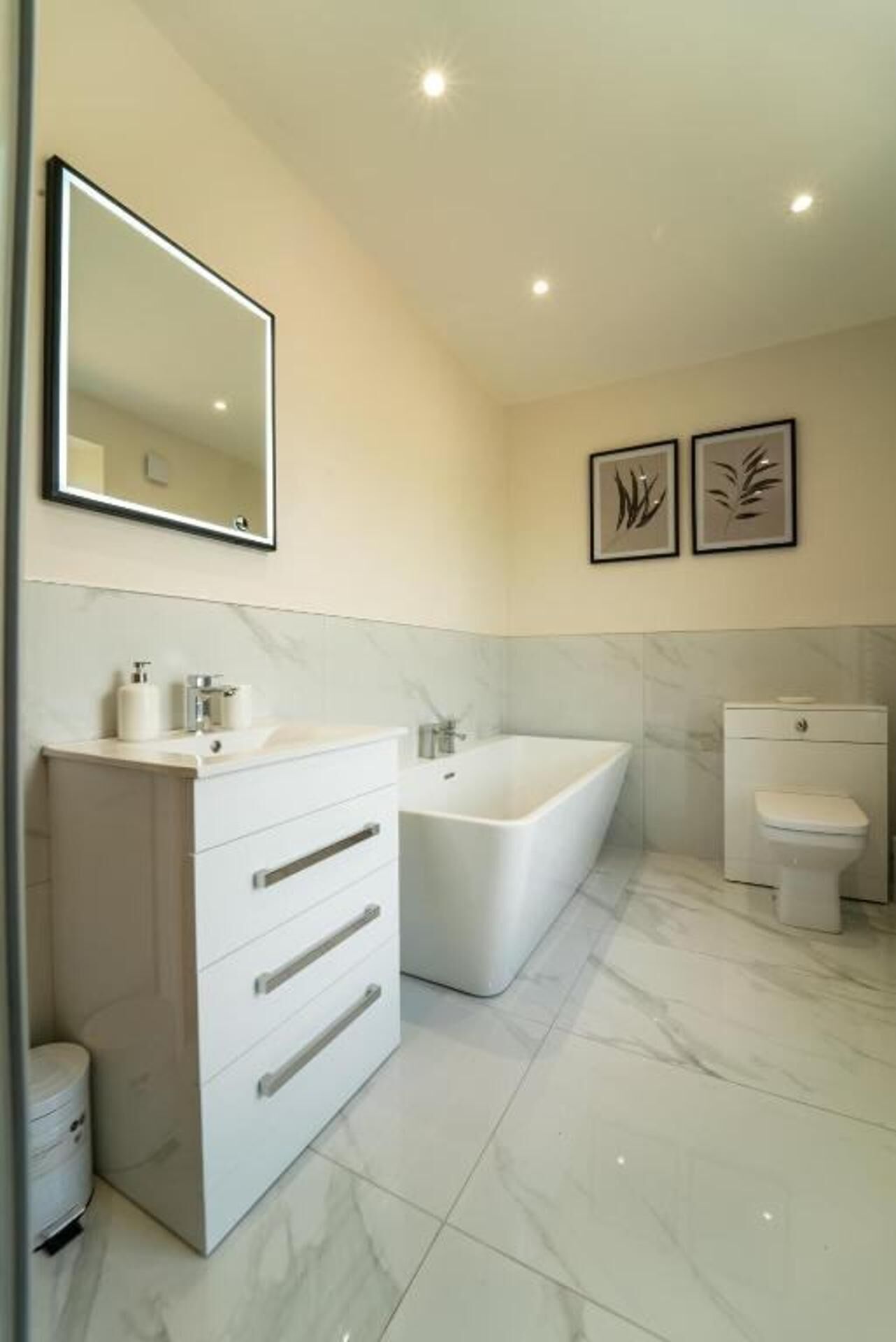 A modern bathroom with a large mirror, a freestanding bathtub, a toilet, and a vanity with drawers.