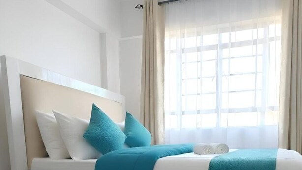 Een moderne hotelkamer met een bed, witte muren, een raam met gordijnen en een hoofdeinde.