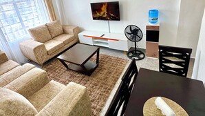 Een moderne woonkamer met een bank, salontafel, televisie en een eethoek met stoelen en een tafel.