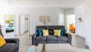 Ein modernes Wohnzimmer mit einem grauen Sofa, bunten Kissen, einem gemusterten Teppich und einem Couchtisch aus Holz.