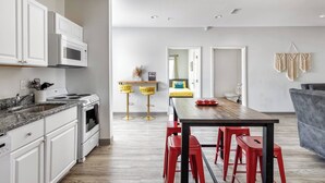 Eine moderne Küche mit weißen Schränken, einer Granit-Arbeitsplatte und einem Edelstahlherd. Es gibt einen Essbereich mit einem Holztisch und roten Barhocker.