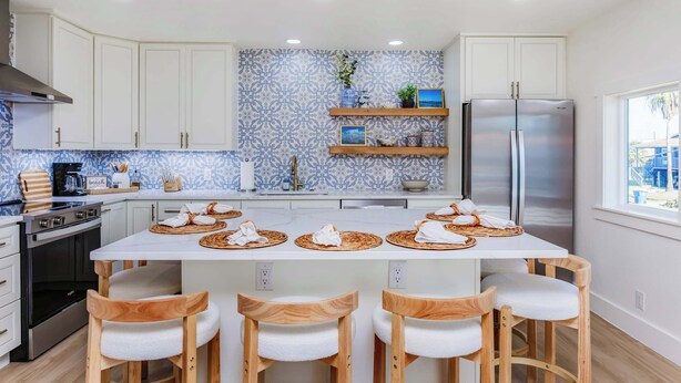 Een moderne keuken met witte kasten, een roestvrijstalen koelkast en een centraal kookeiland met barkrukken.
