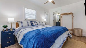 Een slaapkamer met een bed, nachtkastjes, een plafondventilator en een raam met jaloezieën.