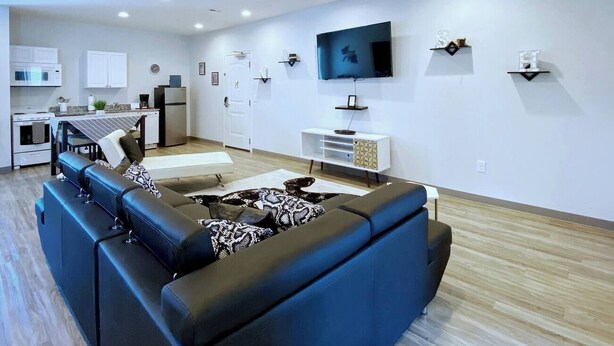 A modern living room with a sectional sofa, a flat-screen TV, and a kitchen in the background. - 🔥 Ring of Fire Retreat — Johnny Cash Hideaway Walkable East Nashville 🖤🎸 (Nashville)