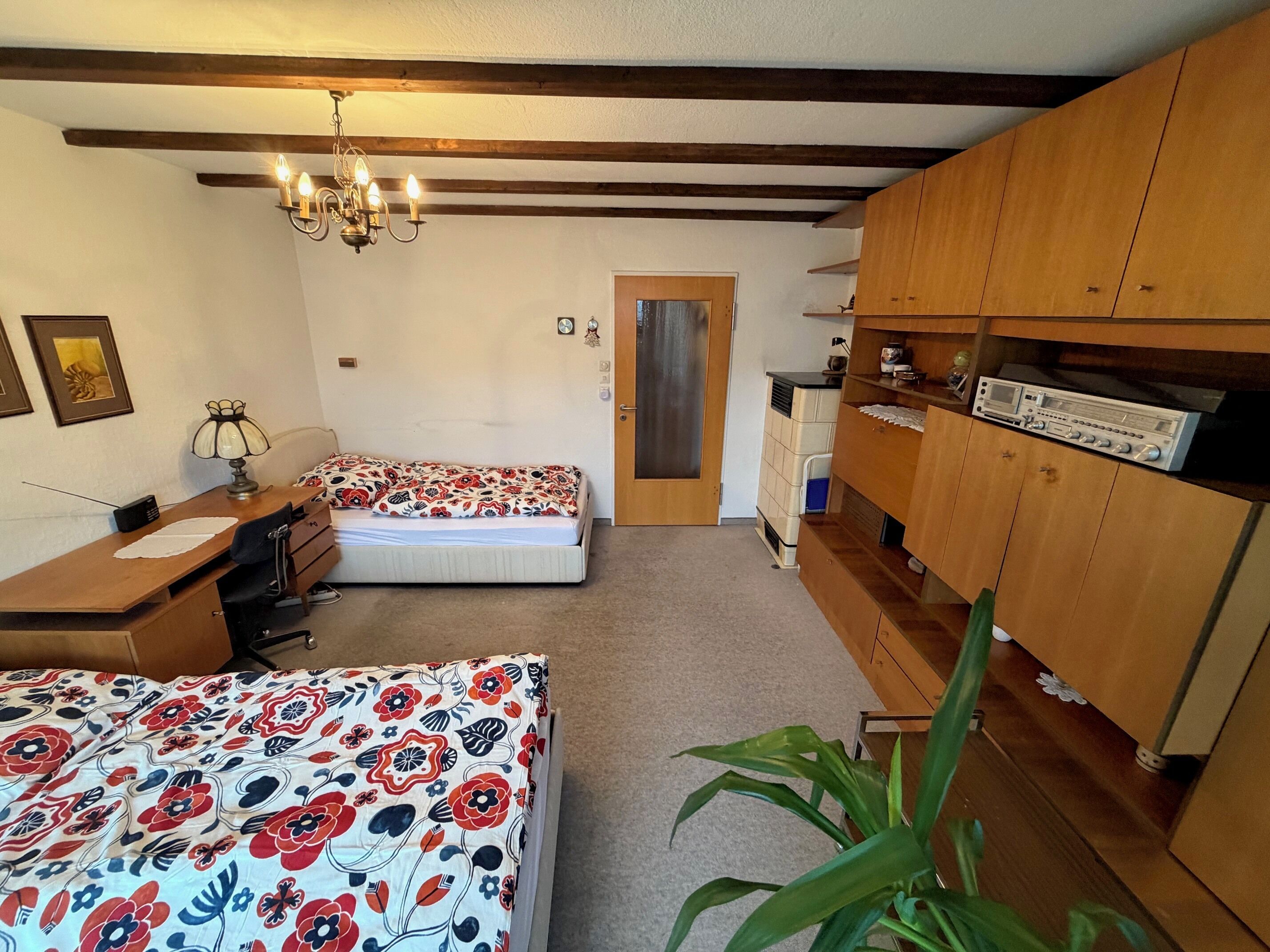A bedroom with two beds, wooden furniture, a chandelier, a wardrobe, and a small desk with a lamp.