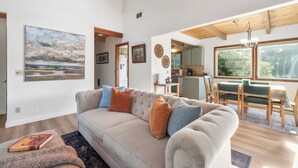Una sala de estar con sofá, una mesa de comedor con sillas, una zona de cocina y un ventanal grande.