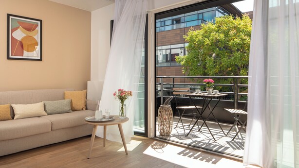 Un salon moderne avec un canapé, une petite table ronde et un balcon équipé d’une table et de chaises.