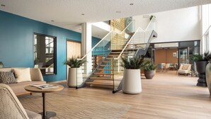 Un hall d’entrée spacieux, doté d’un escalier, d’un espace salon et de plantes en pot.