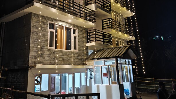 A multi-story building with balconies, string lights, and a reception area. - Hils & Paw (Manali)