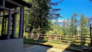 A wooden deck with a view of a mountainous landscape. - Hils & Paw (Manali)