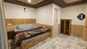 A bedroom with a wooden headboard, a bed with a patterned blanket, a nightstand, a wardrobe, and a door. - Hils & Paw (Manali)