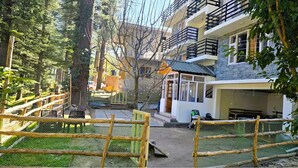 A residential building with a fenced yard, a small porch, and a vehicle parked outside. - Hils & Paw (Manali)