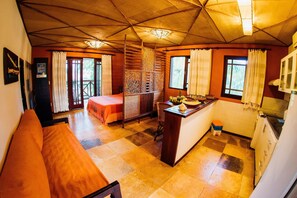 A room with a wooden bench, a bed, a small kitchen area, and a balcony with a view.