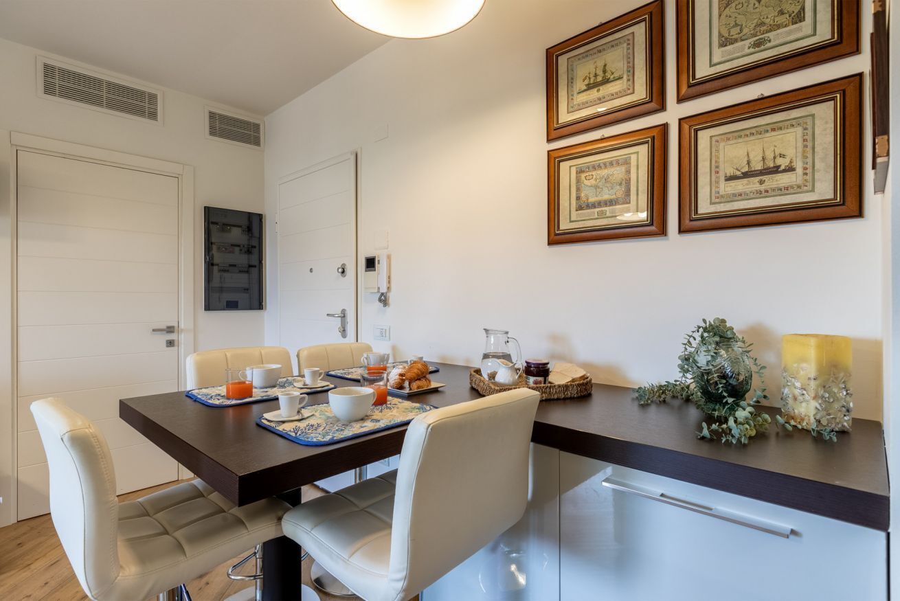 A dining area with a table set for breakfast, including plates, cups, and a pitcher. There are framed pictures on the wall and a decorative candle on the table.