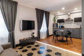 Ein modernes Wohnzimmer mit Flachbildfernseher, einem Essbereich mit rundem Tisch und Stühlen sowie einer Küche mit Mikrowelle und Pflanze.