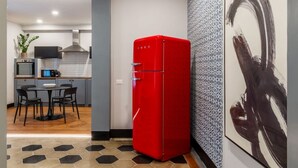 Eine moderne Küche mit einem roten Kühlschrank, einem Essbereich mit rundem Tisch und Stühlen sowie einer Wand mit Muster.