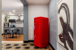 Eine moderne Küche mit einem roten Kühlschrank, einem Essbereich mit rundem Tisch und Stühlen sowie einer Wand mit Muster.